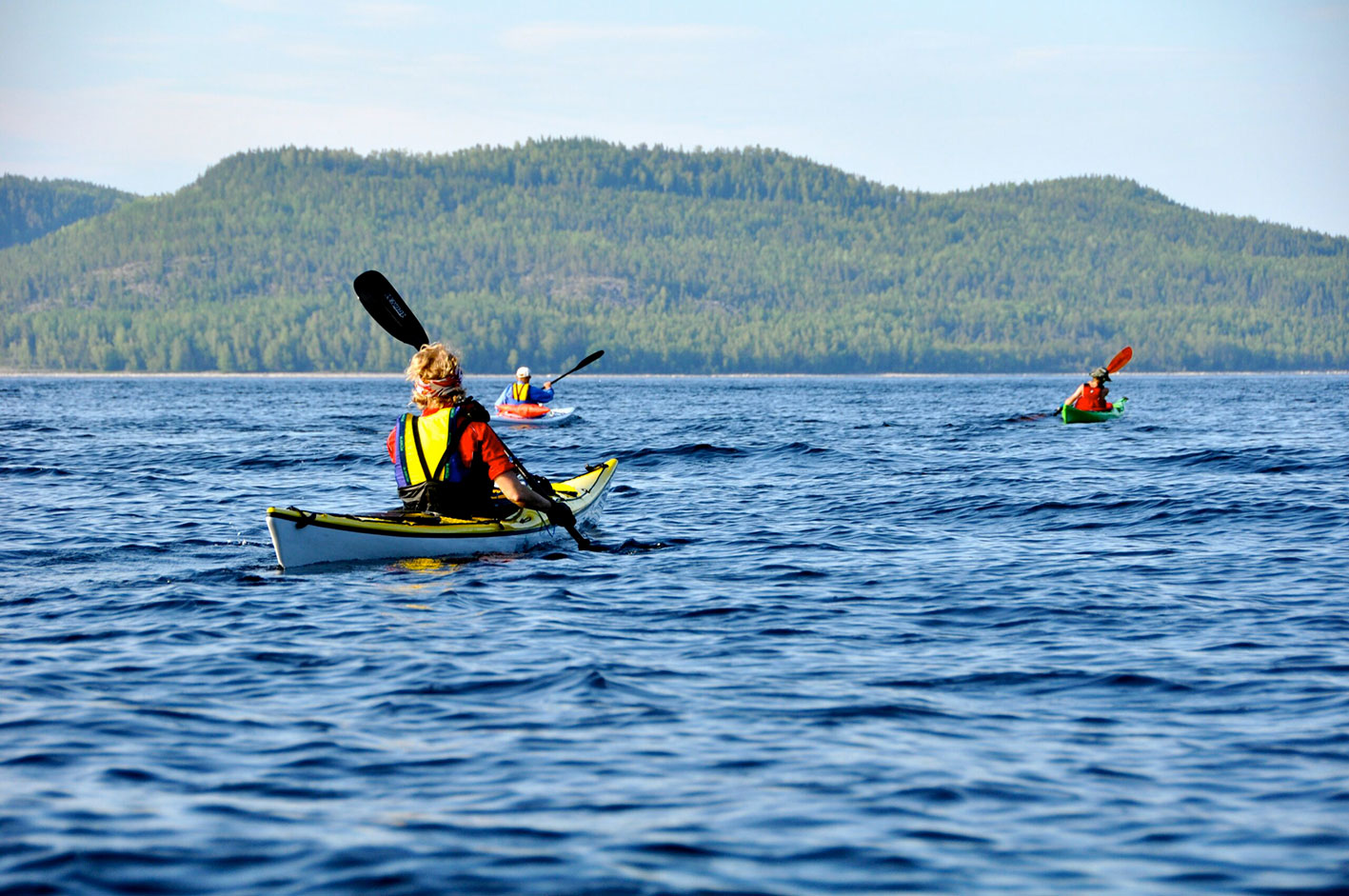 Tre personer paddlar havskajak på havet en solig dag på Höga Kusten.